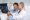 A concerned mid adult father points to a set of x-rays as a pediatrician shows him the images and shares the discovery.  They are standing in an exam room.  His teen daughter sits on a bed in the background.